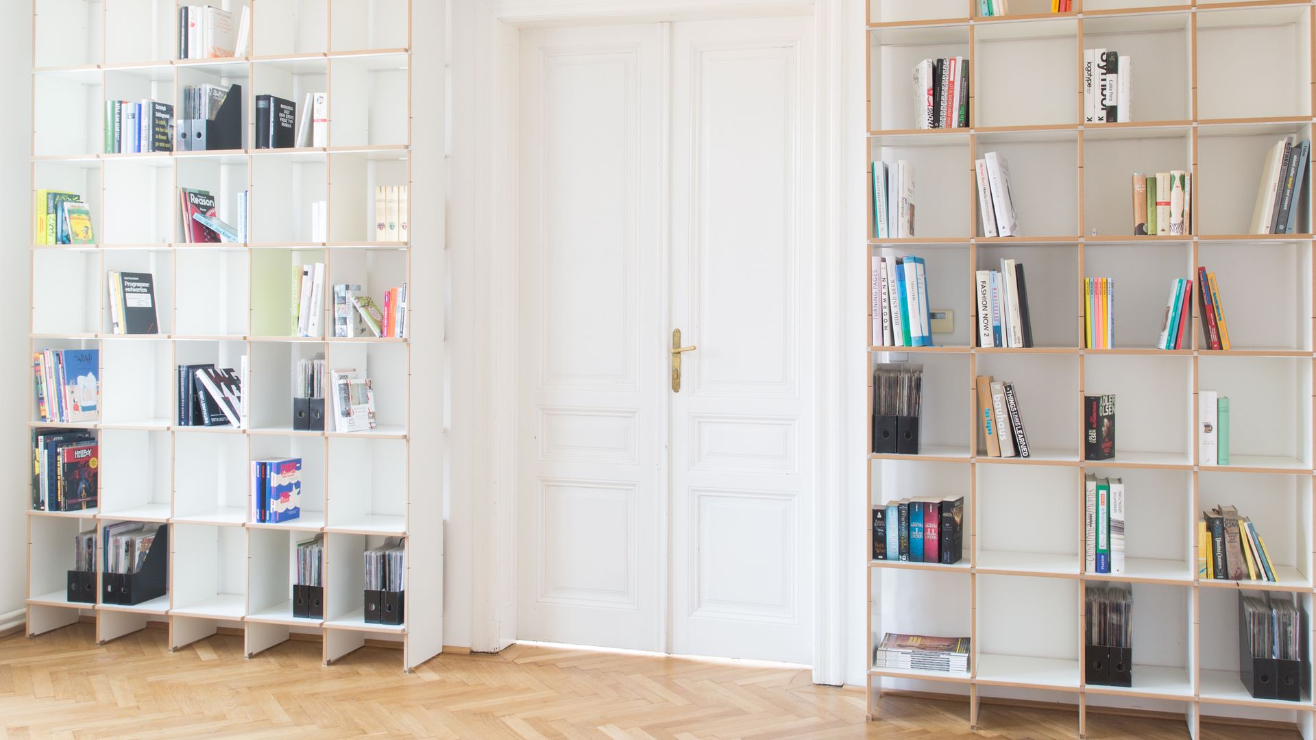 Salón con suelo de madera, librería que bordea la puerta de paso y llega hasta el techo, con libros