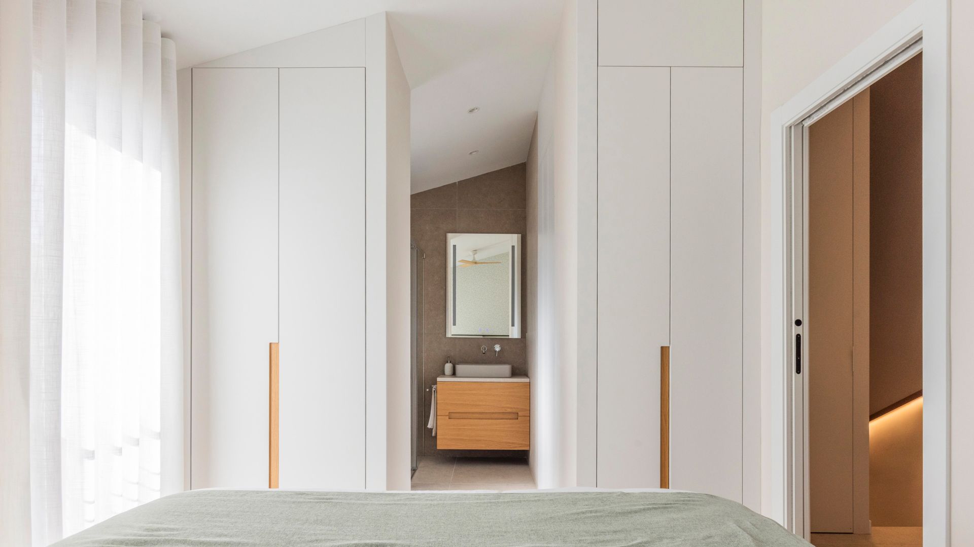Dormitorio en suite con armarios blancos hasta el techo 
