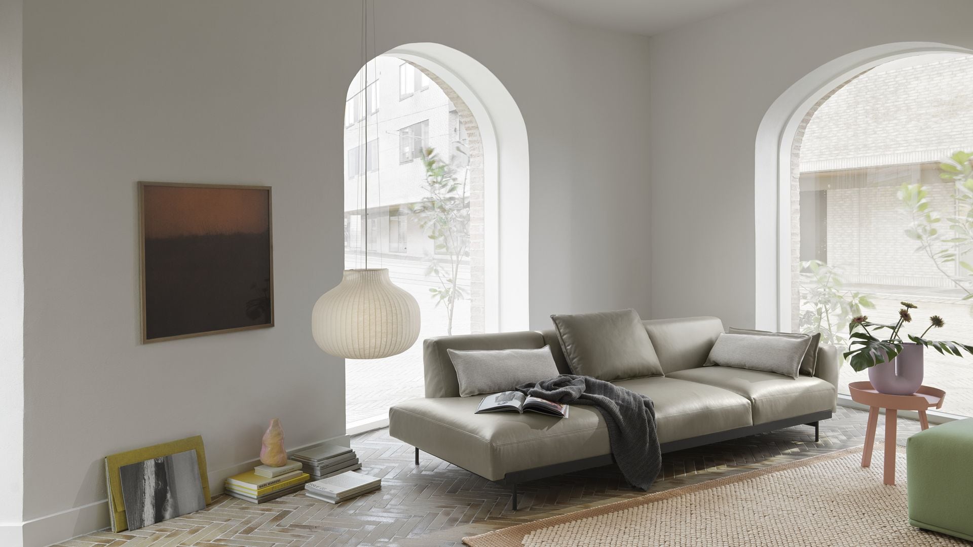 Salón con sofá gris de cuero, alfombra, lámpara de techo de papel y ventanas en arco