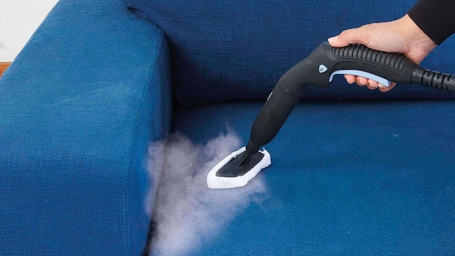 Una mujer limpiando un sofá con un limpiador a vapor
