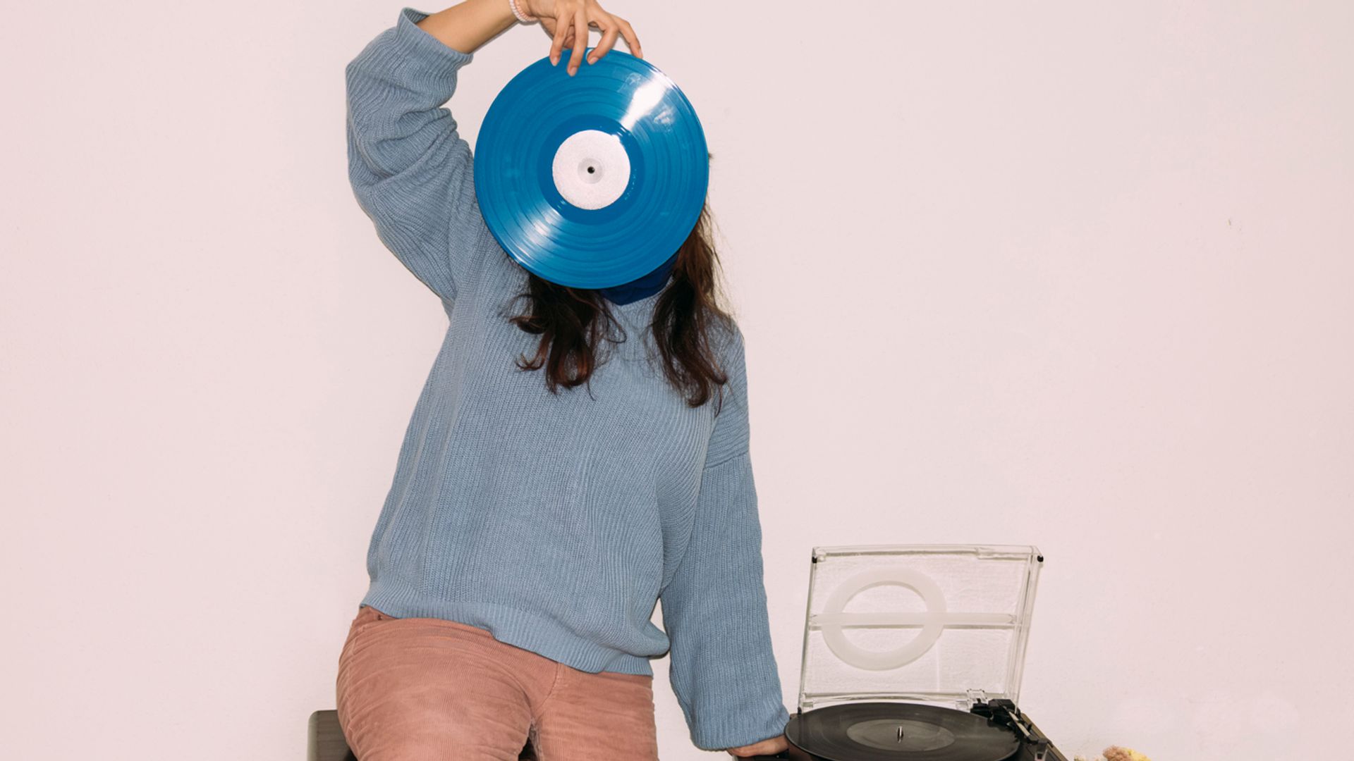 Una mujer escuchando música en casa, sentada junto a su tocadiscos mientras sostiene un disco de vinilo azul.