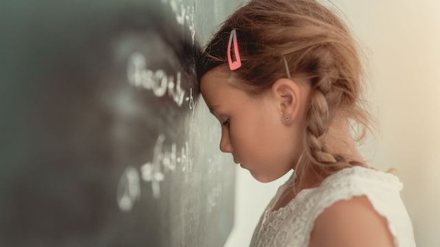 Niña apoyando la cabeza en la pizarra con actitud agobiada