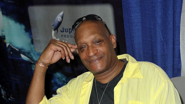 Plano medio de Tony Todd con camisa amarilla y pantalón gris