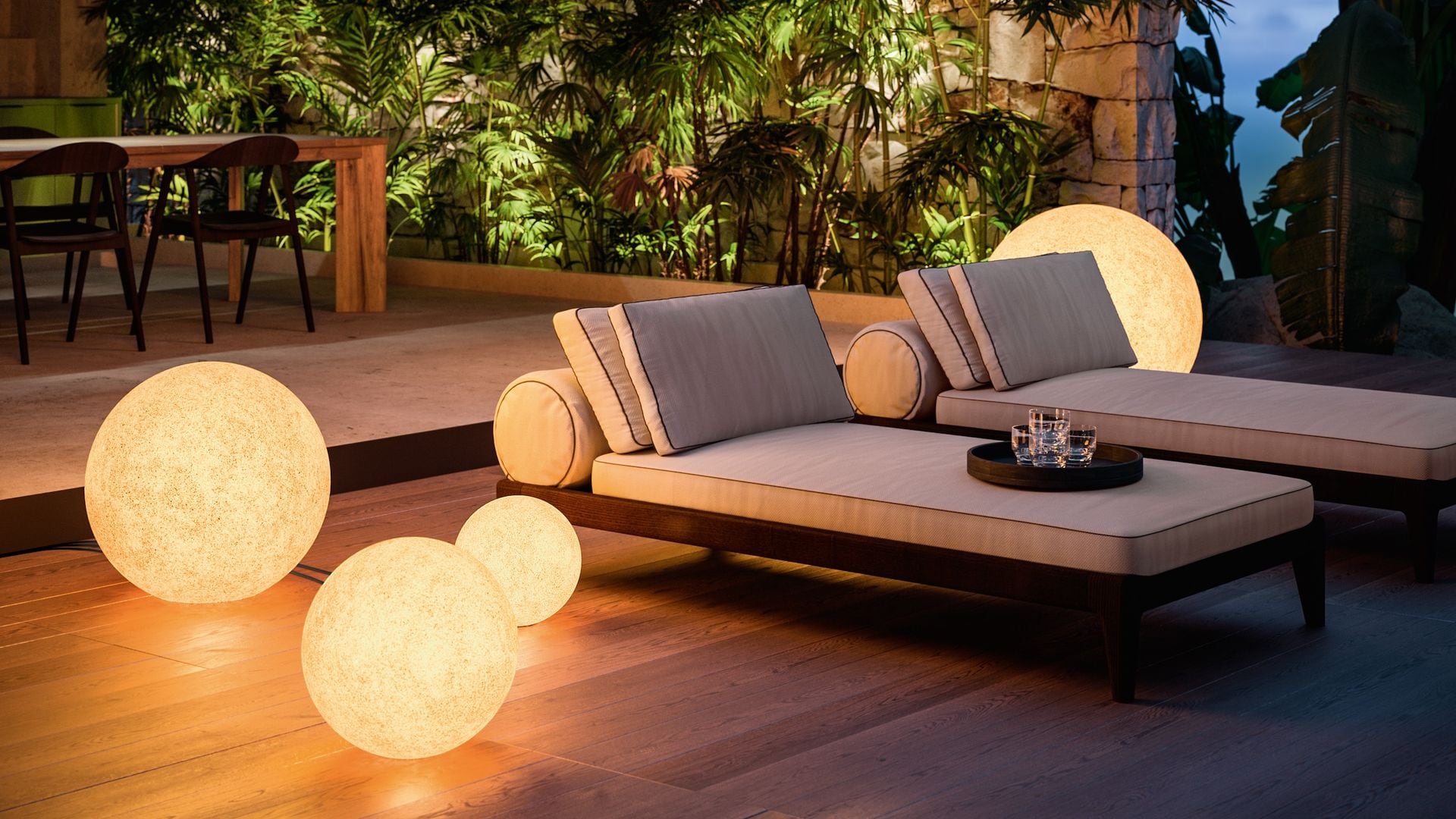 Jardín de noche, con suelo de madera, tumbonas blancas y lámparas de suelo