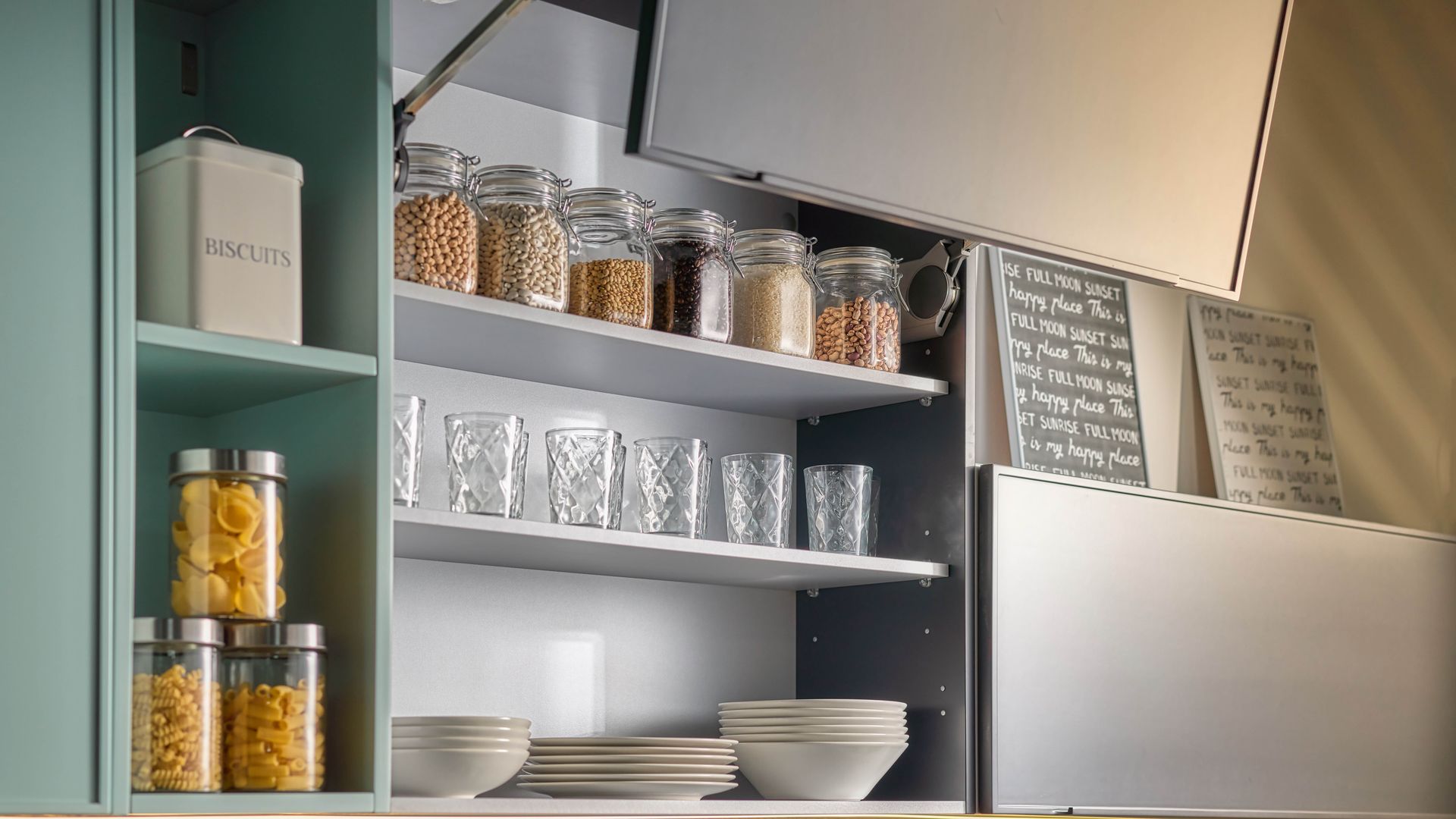 Armario de cocina superior abierto con botes de cristal con comida sea, vajilla blanca y vasos 