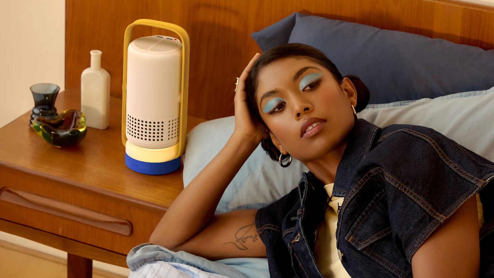 Mujer tumbada en la cama con sombra de ojos azul y el proyector XGIMI Vibe One en la mesilla