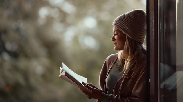 Mujer joven leyendo un libro en otoño en una ventana