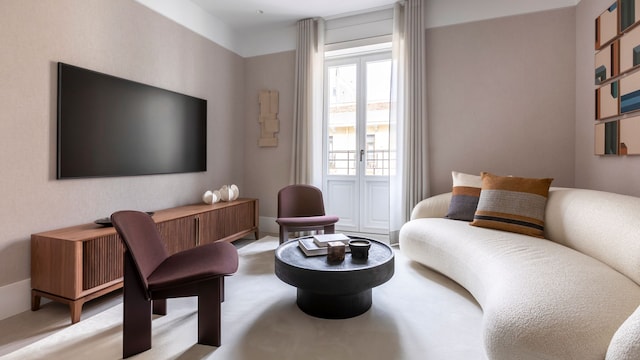 Salón con sofá curvo blanco, alfombra, mesa de centro negra, butacas burdeos, aparador de madera, cuadros y televisión en la pared