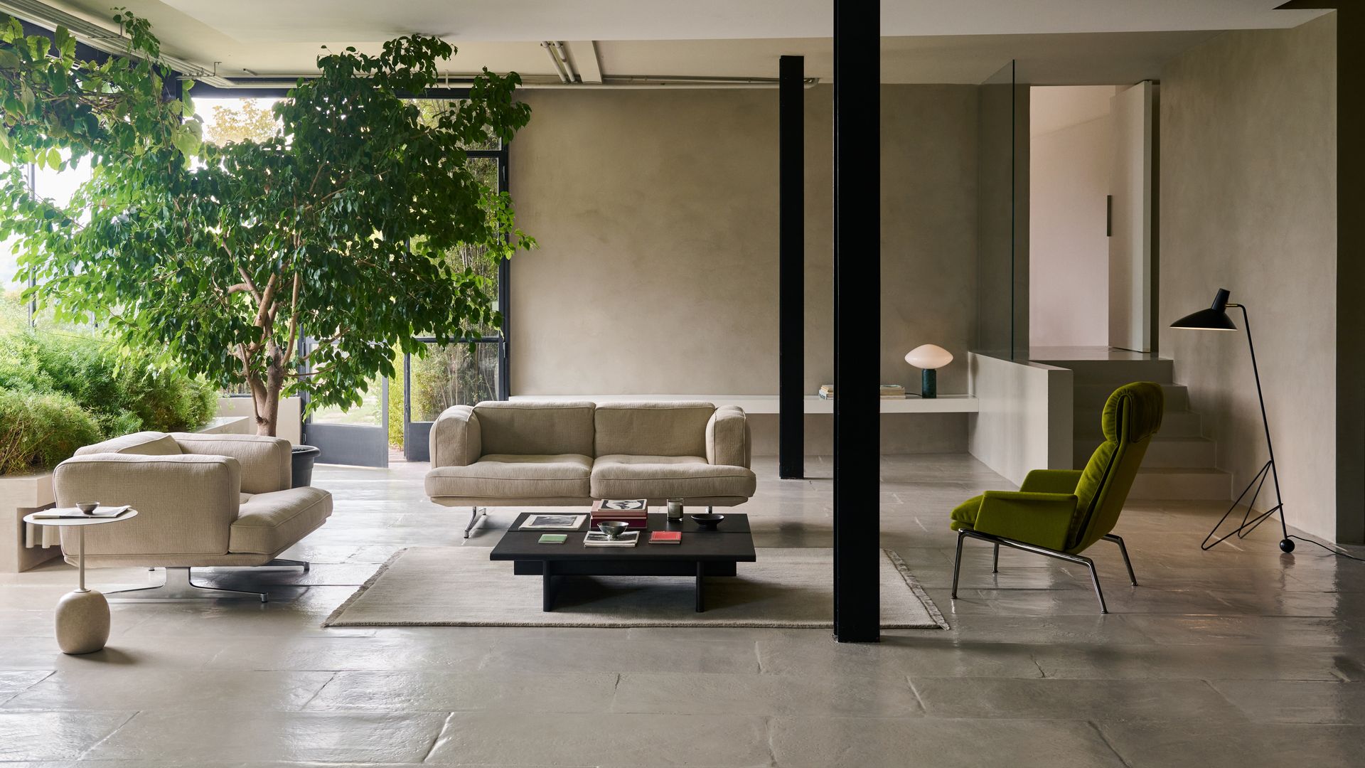 Salón de estilo nórdico comunicado con el jardín, sofás blancos, alfombra, suelo blanco, butaca verde, lámpara de pie negra y lámpara de sobremesa