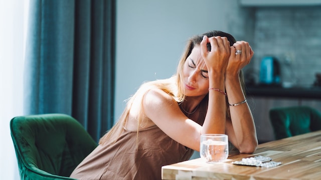 mujer con dolor de cabeza, con pastillas sobre la mesa