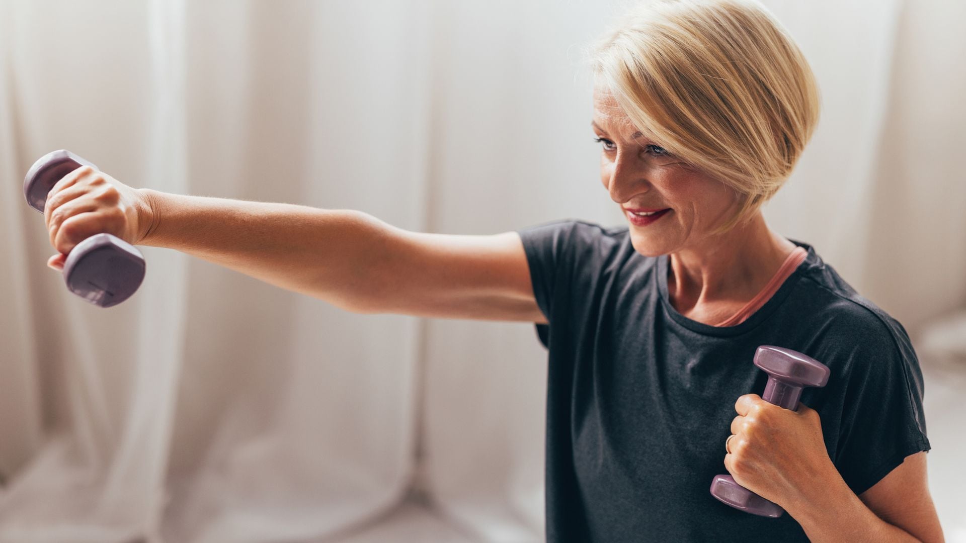 Mujer mayor de pelo rubio corto practicando pesas en casa