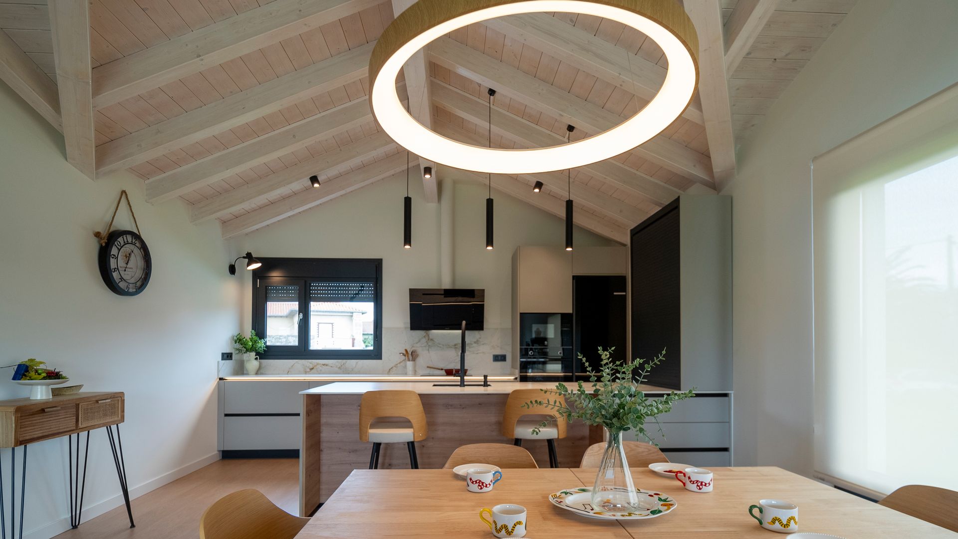 Cocina con comedor, barra con taburetes, muebles grises, consola, lámpara de techo