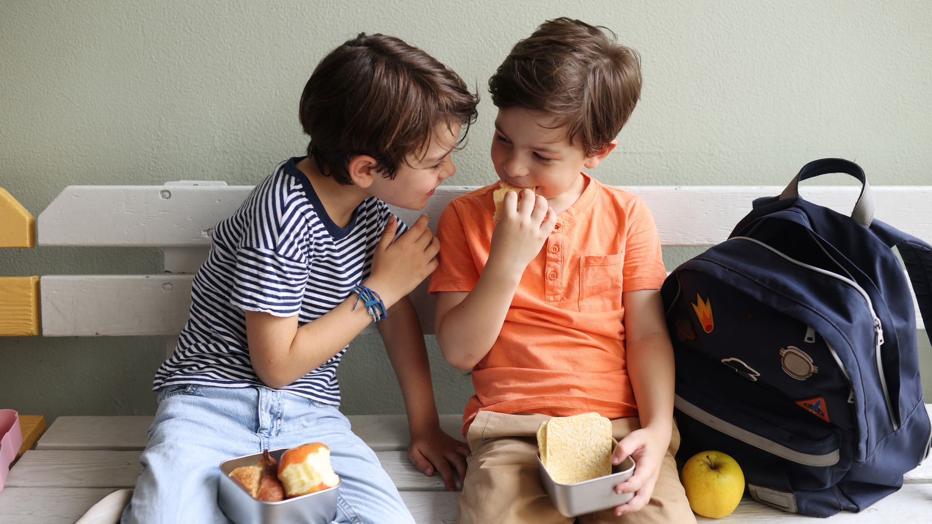 Niños comiendo de un táper en los bancos de un colegio, riéndose entre ellos.