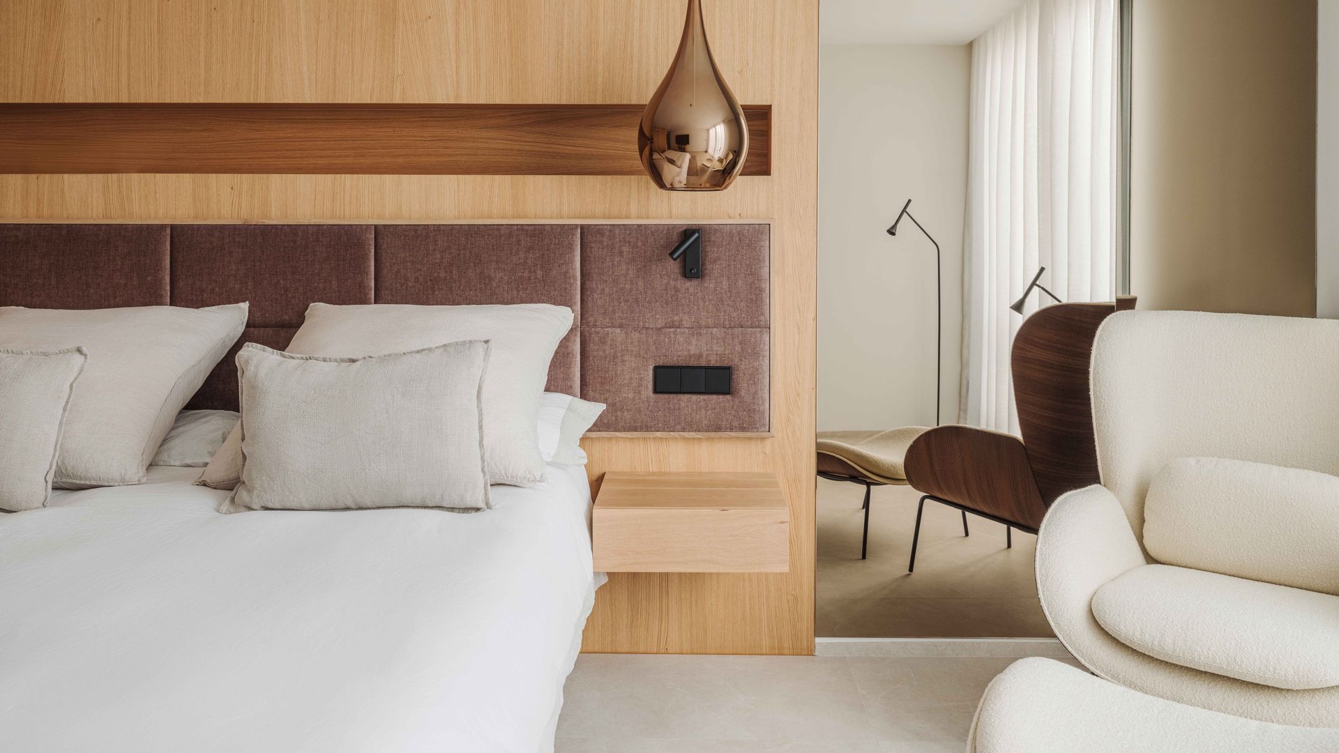 Dormitorio con pared de cabecero de madera, cabecero de cuero, lámpara de techo, butaca 
