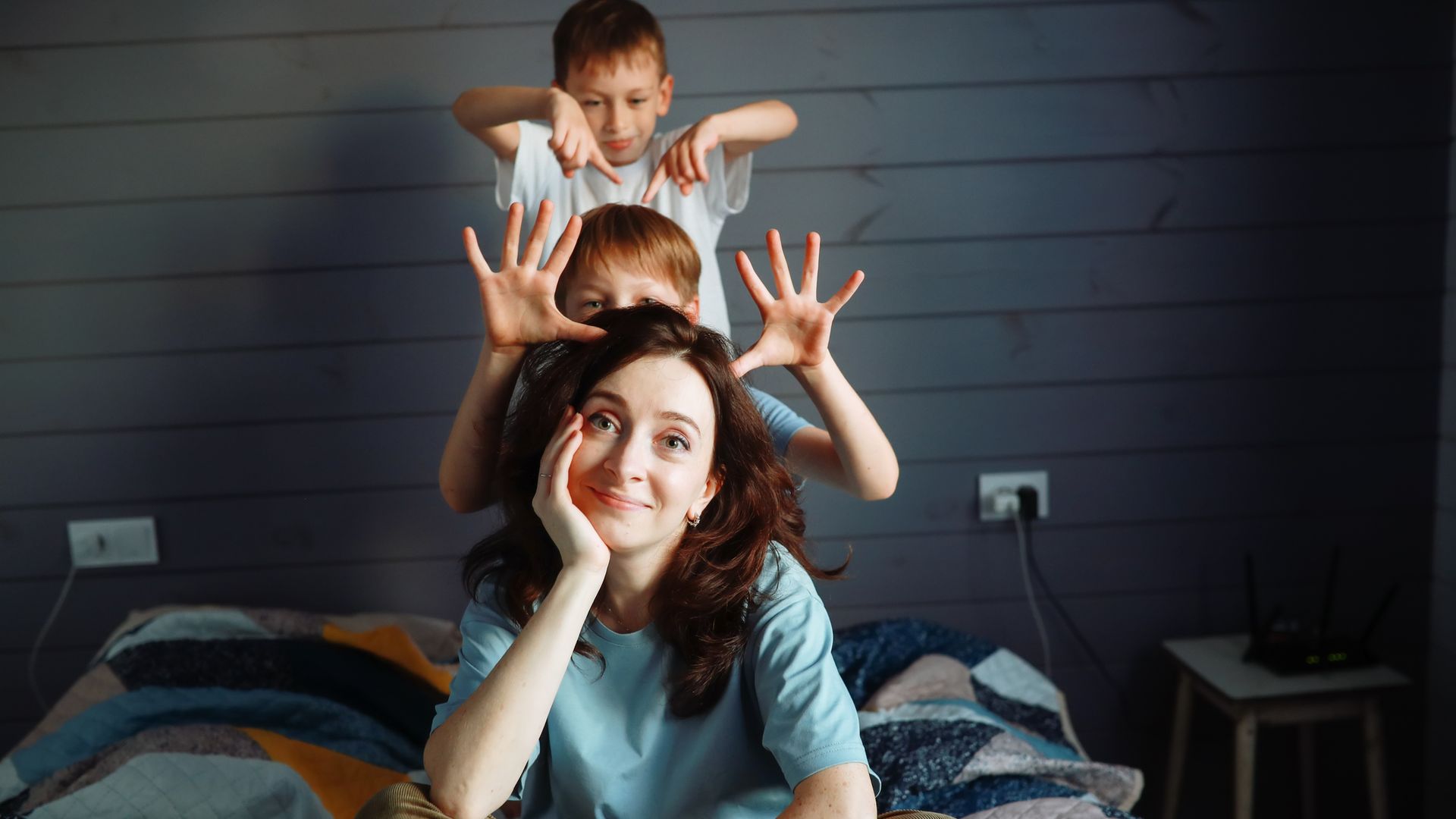 madre sonriente y resignada, sentada en la cama, junto con sus dos hijos pequeños