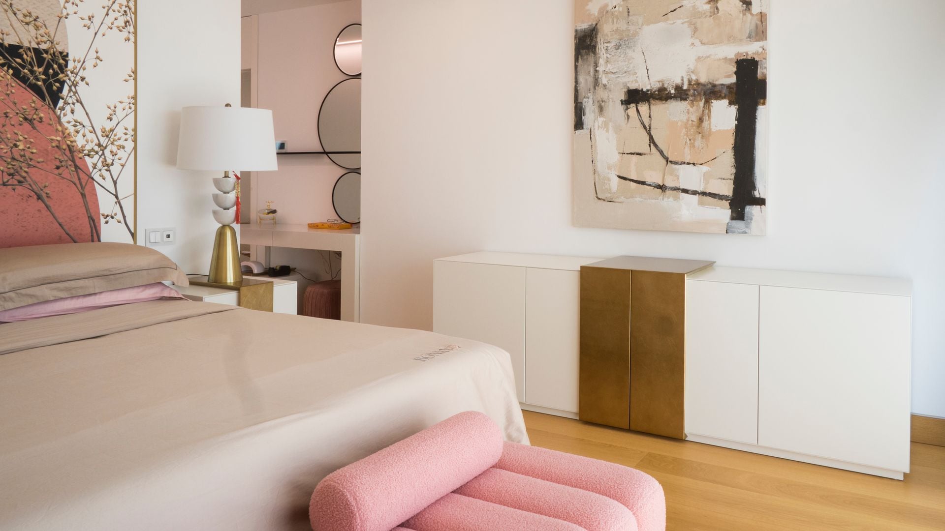 Dormitorio con aparador blanco y dorado y zona de tocador con cuadro, banqueta rosa