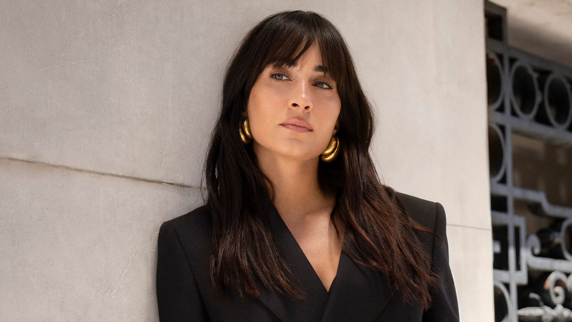 Aitana con traje de chaqueta negro, el pelo suelto y accesorios dorados en la calle