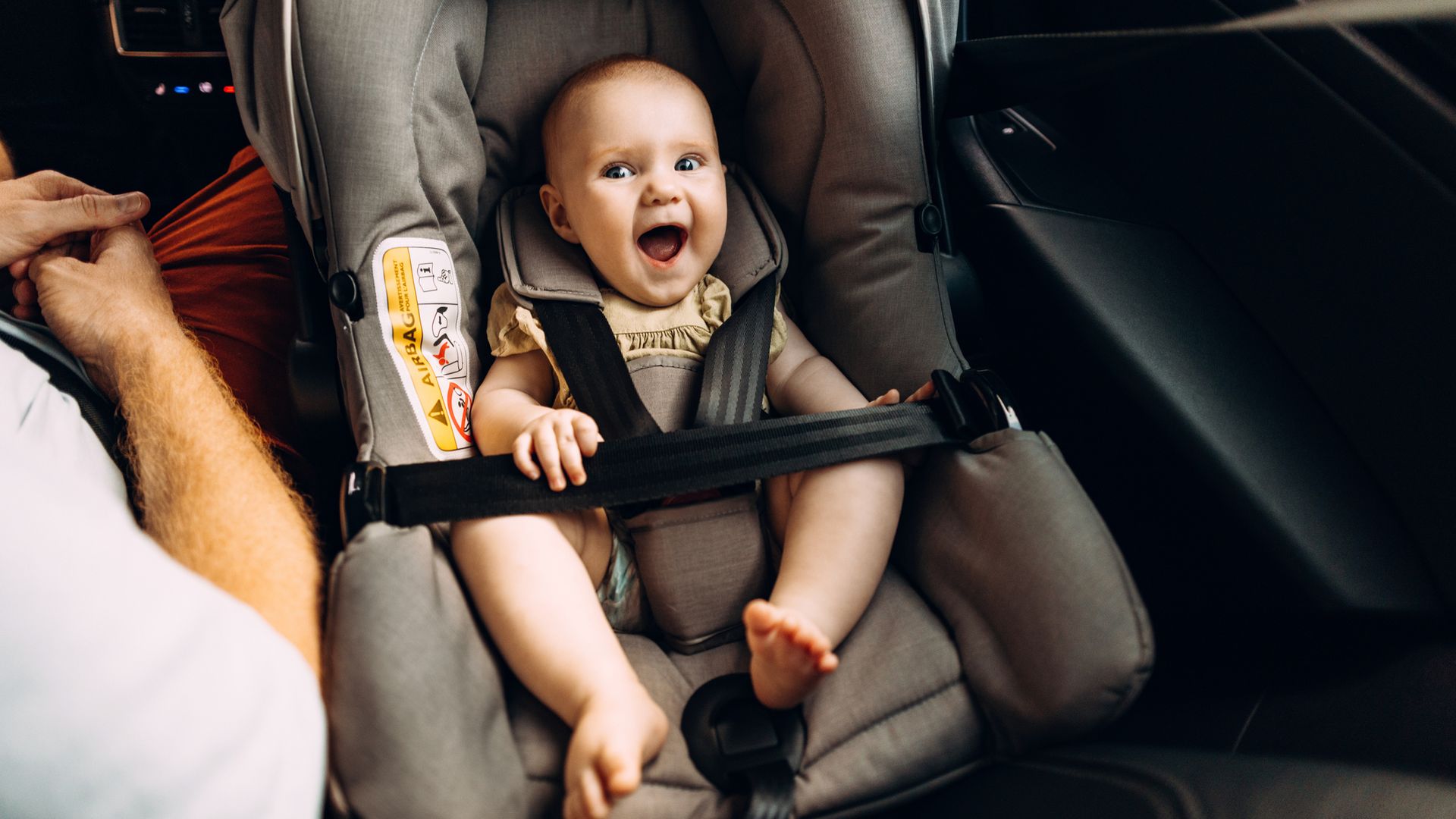 Bebé sonriendo feliz en la silla de coche de bebé dentro de un coche mientras está sentado a su lado su padre.