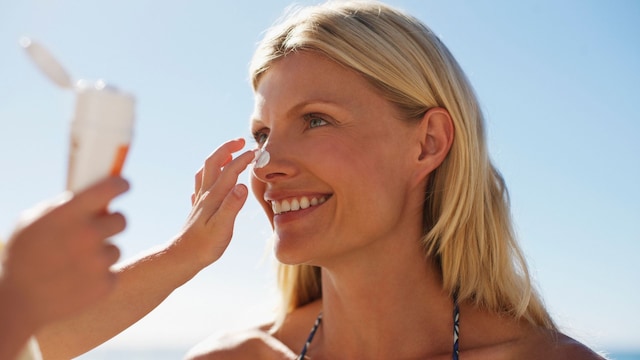 Rostro de mujer rubia sonriente mientras un niño le aplica crema solar en la nariz