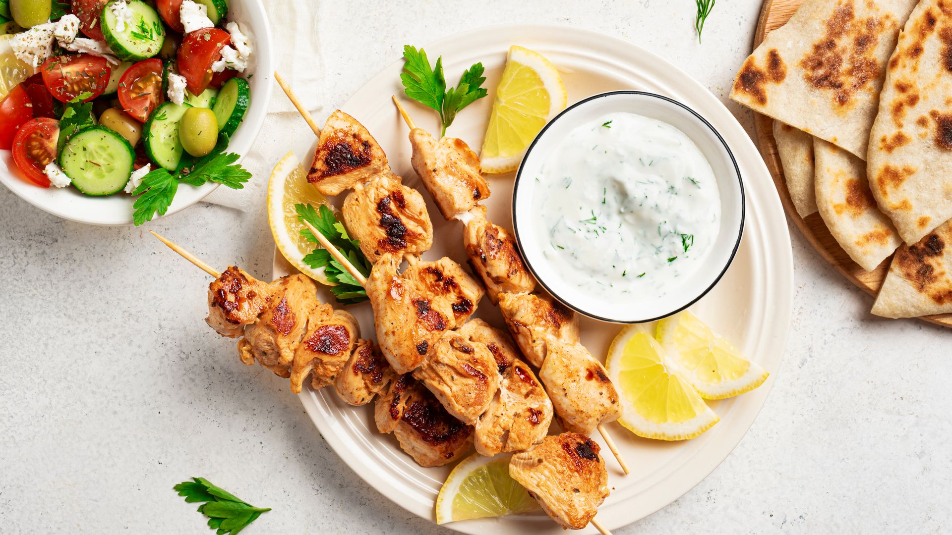 Brochetas de pollo con salsa tzatziki y ensalada.