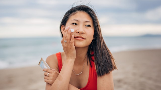 Mujer asiática aplicándose crema solar en el rostro en la playa