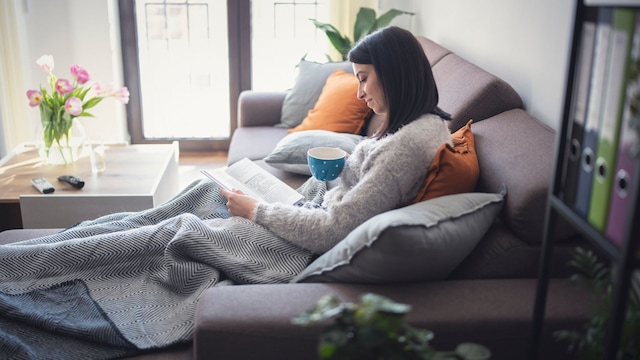 mujer leyendo un libro con un café en casa, sentada en el sofá