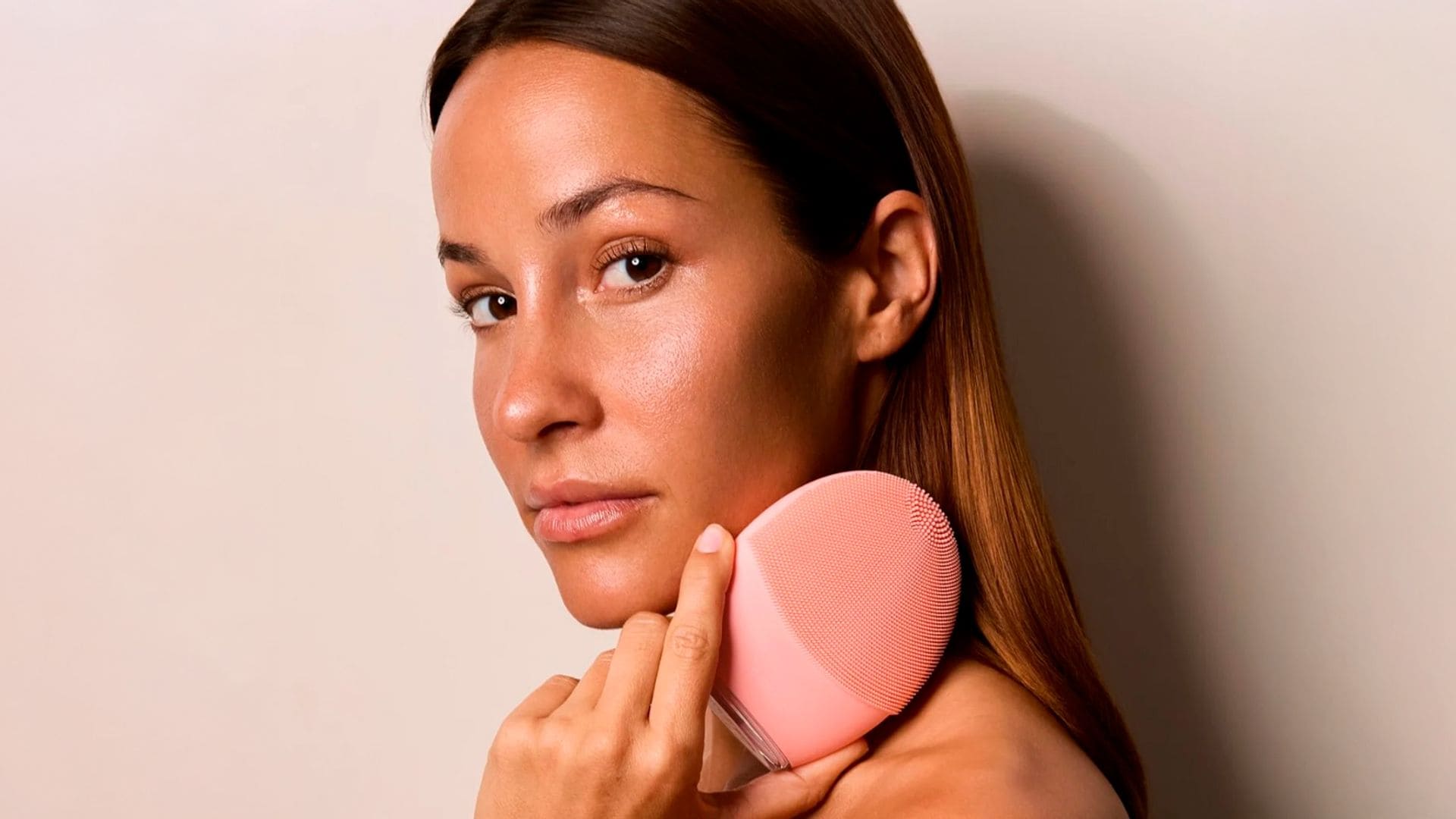 Rostro de mujer morena con pelo castaño con cepillo facial de FOREO en la mano
