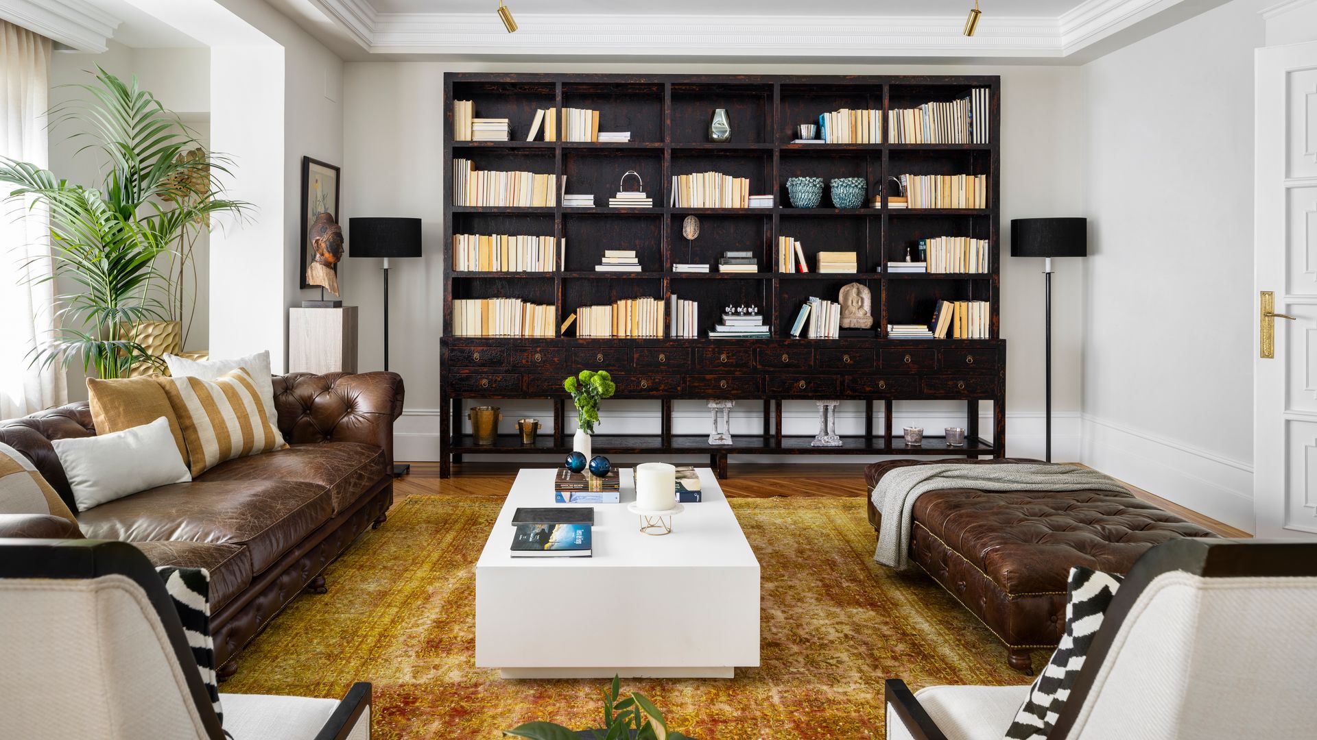Salón con sofás de cuero marrón, alfombra mostaza, librería de madera oscura, mesa de centro blanca