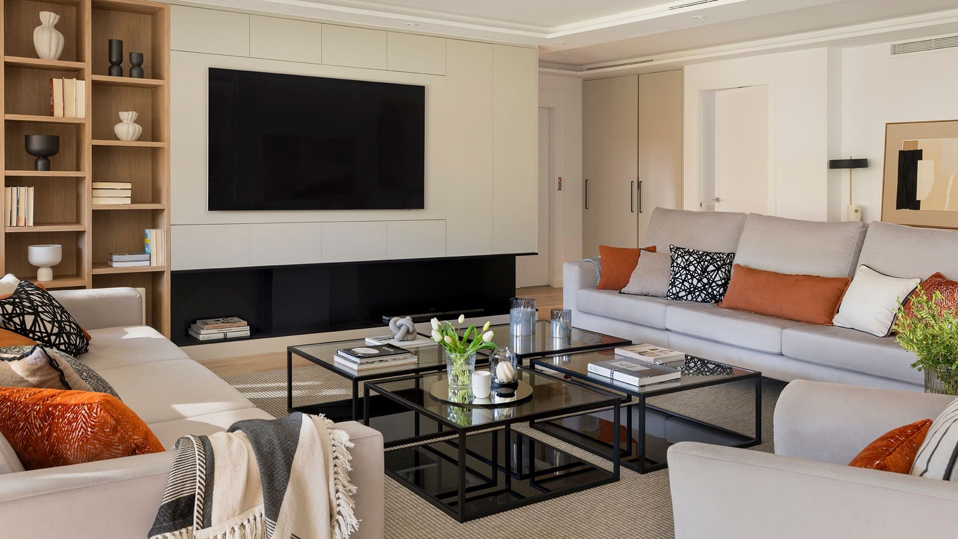 Salón con entrada directa de la calle, sofás grises, mueble a medida para el televisor, cuatro mesas negras de centro