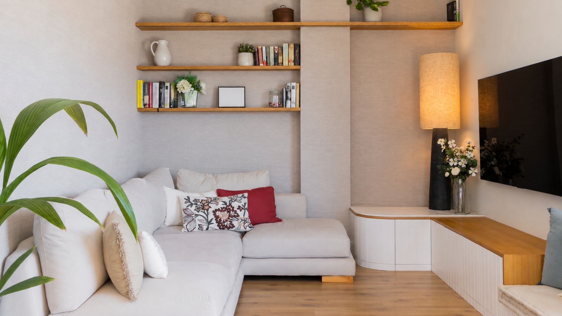 Salón con baldas de madera con libros y adornos, sofá beige, lámpara de pie negra, cojines en el sofá