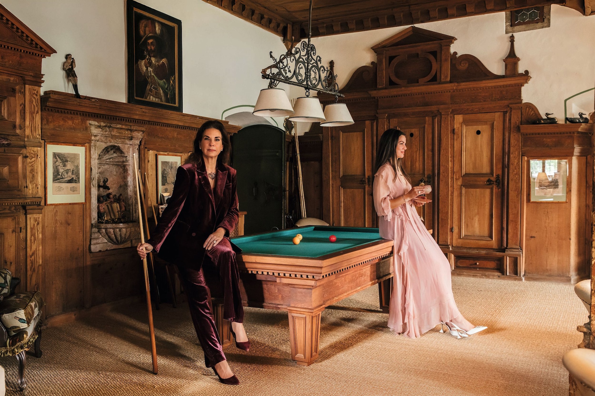 Dos mujeres en una sala de billar, una sentada con tacones y la otra de pie con sandalias.