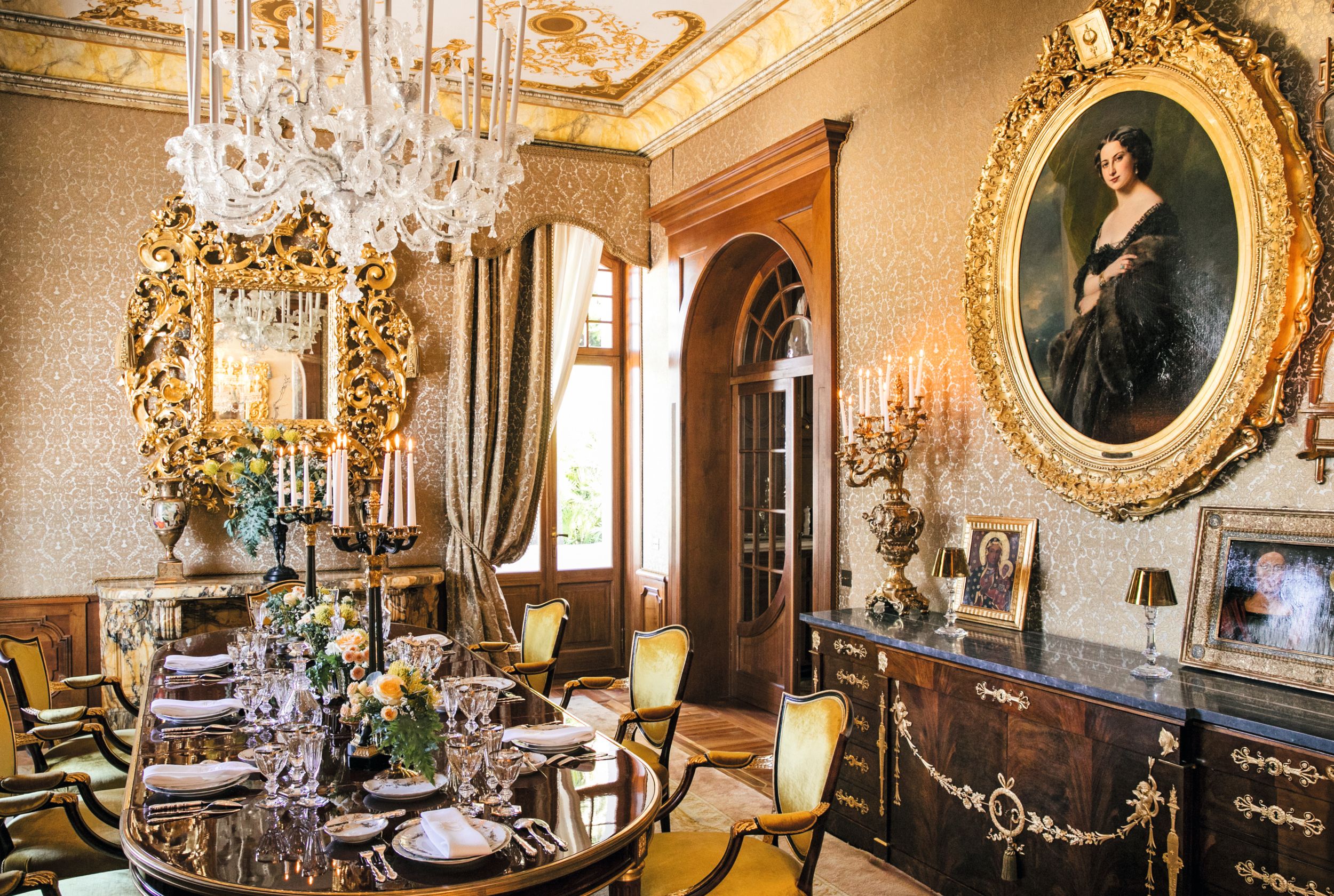 La mesa está dispuesta con copas de Baccarat estilo Empire, platos de porcelana de Bernardaud y candelabros de estilo imperio. Sobre el aparador cuelga un retrato ovalado de Winterhalter de la baronesa Octavie de Löwenthal