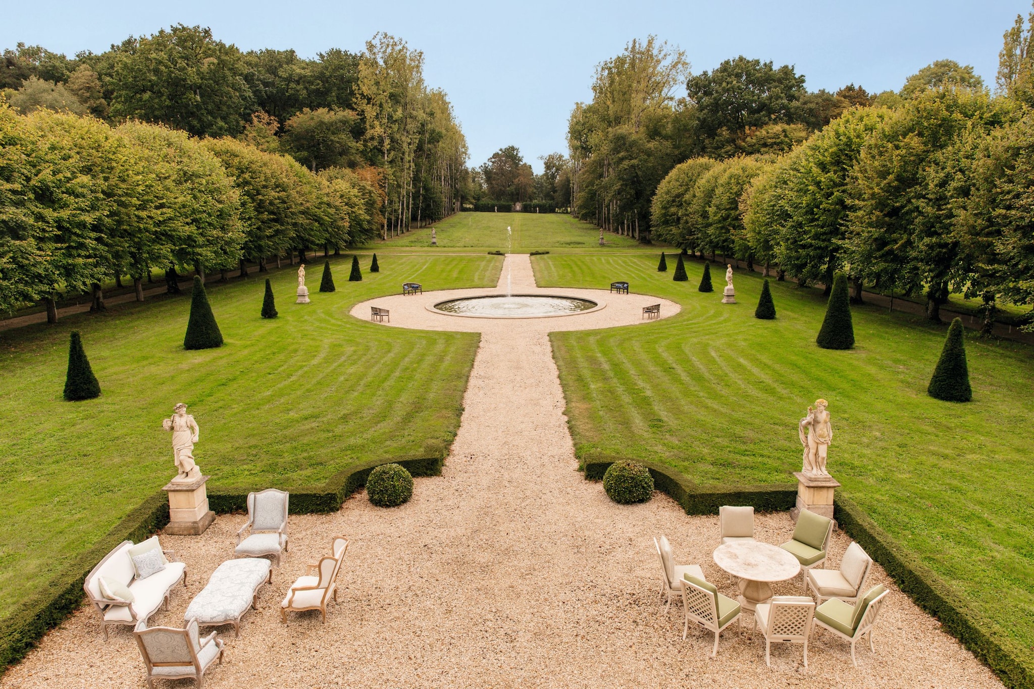 Vista aérea de un jardín formal con muebles de exterior, estatuas y fuente central