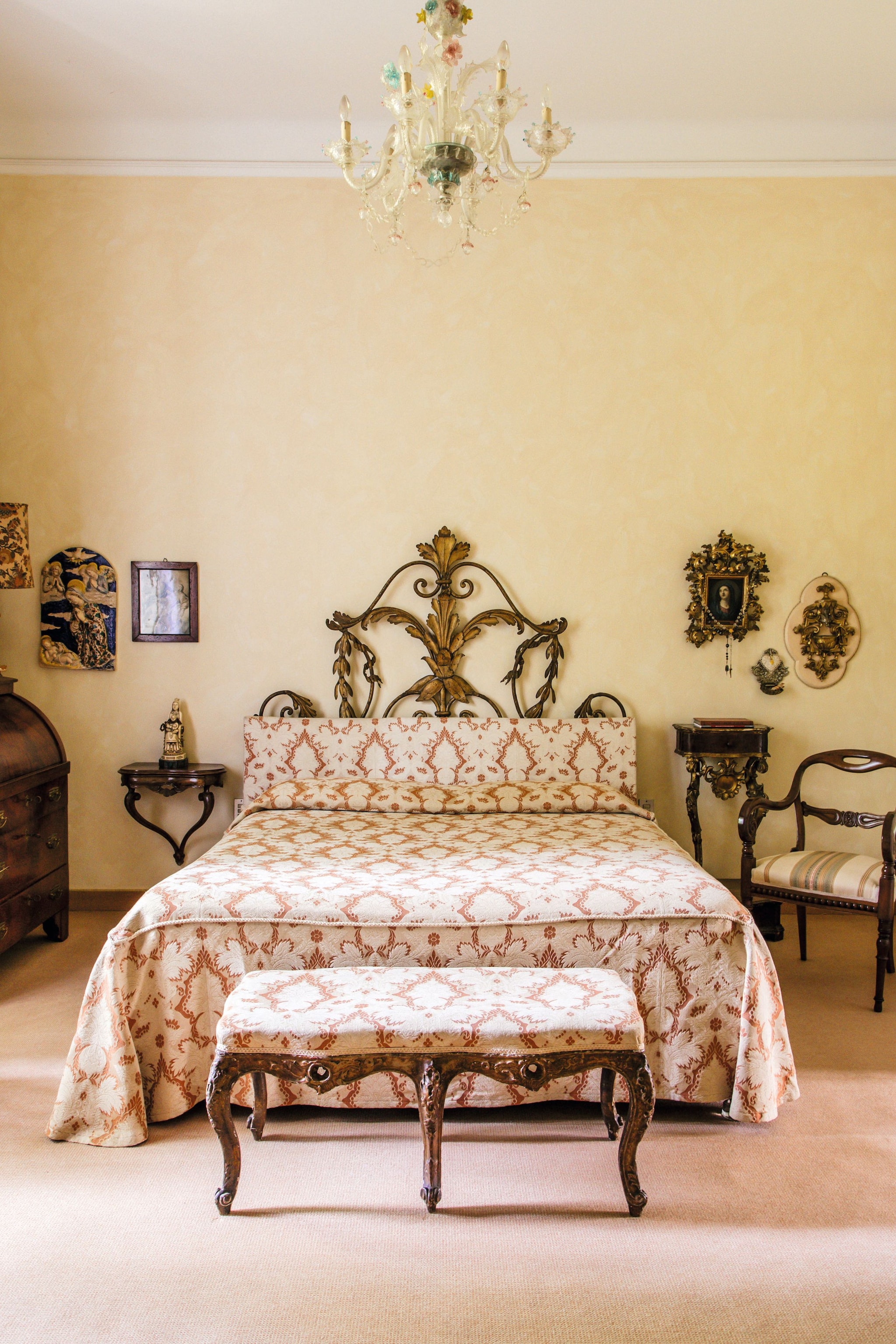 El dormitorio principal de la casa, con cabecero con cama en madera y metal de estilo floral, del siglo XVIII. La lámpara es de cristal de Murano y las paredes están decoradas con imágenes religiosas