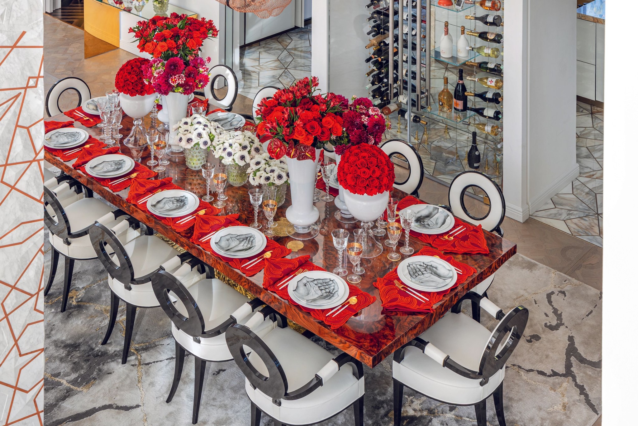 Mesa larga con sillas, mantel rojo, flores y vajilla en un comedor elegante.