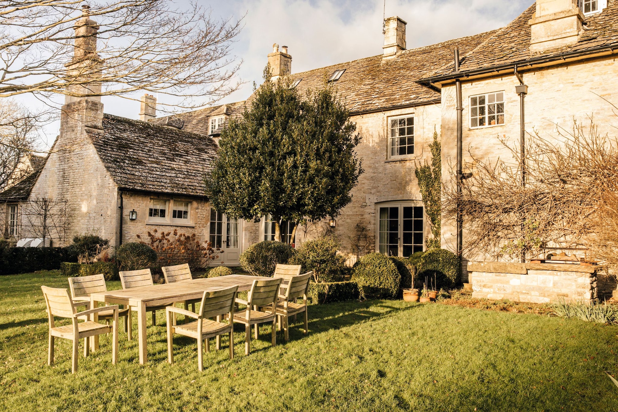 Casa antigua con chimeneas, mesa de madera y sillas en el césped.
