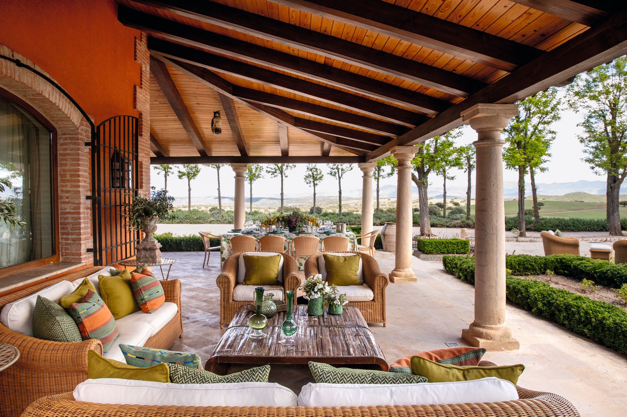 El porche, que cuenta con varias zonas de descanso y una gran mesa de comedor con vistas al jardín y la piscina