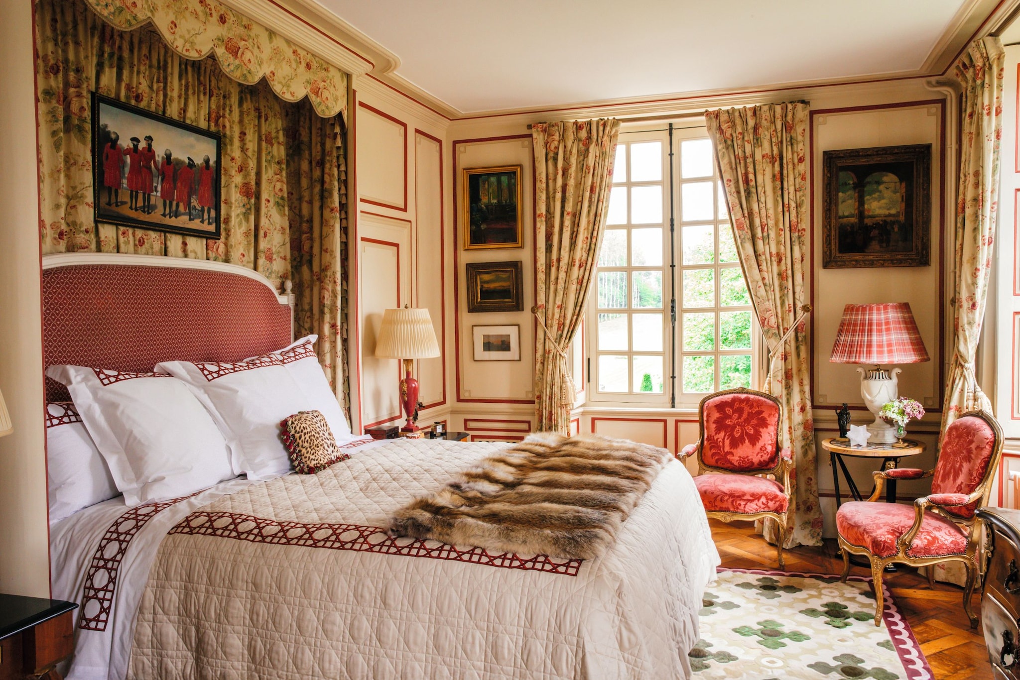 Habitación con cama grande, sillas rojas, y ventana con cortinas florales.
