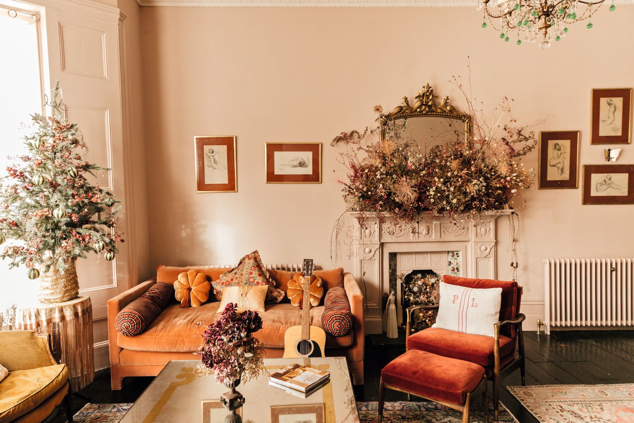 Sala de estar elegante con sofá naranja, silla roja, chimenea decorada y árbol de Navidad.