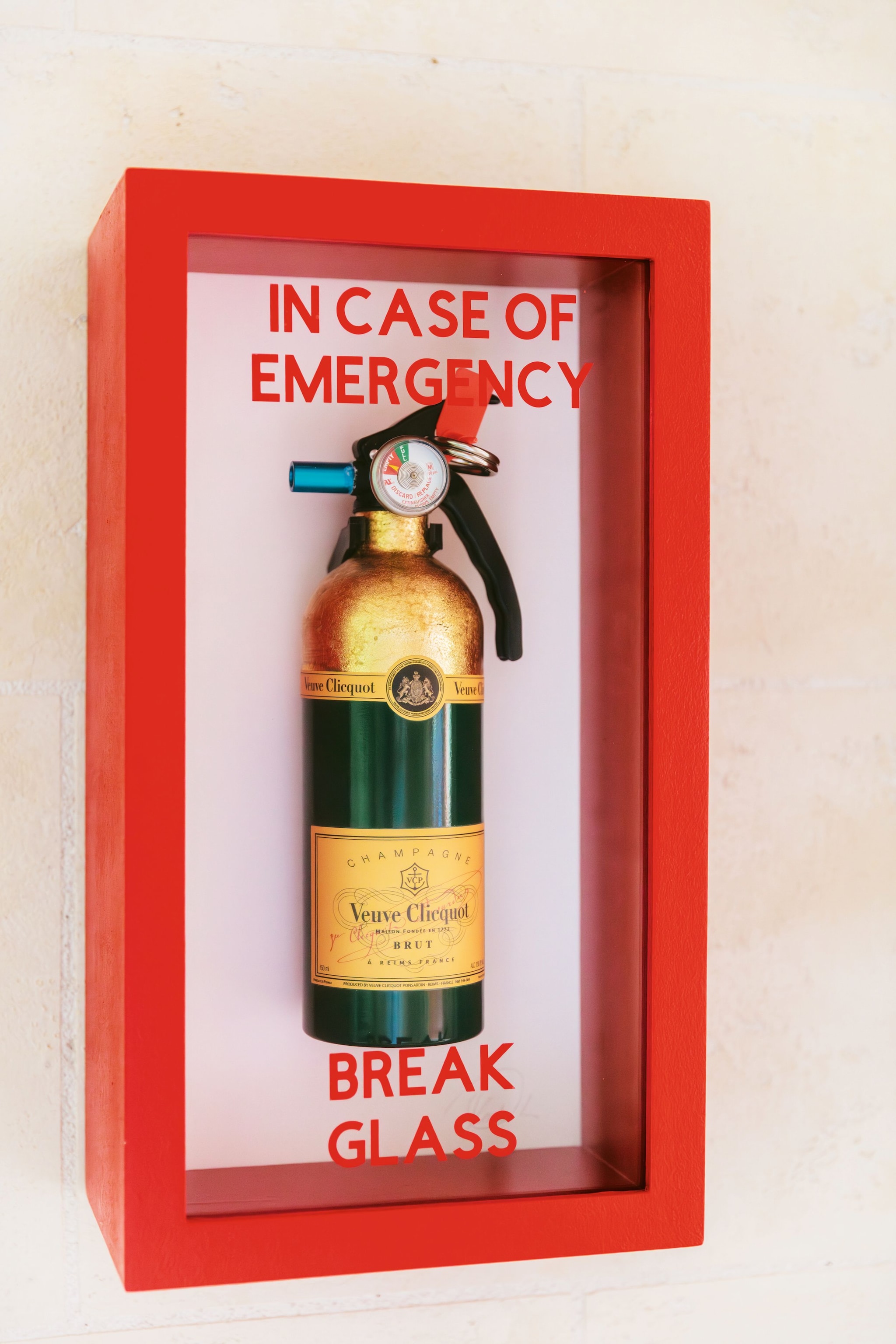 Botella de champán Veuve Clicquot en caja roja que imita un extintor con texto "IN CASE OF EMERGENCY BREAK GLASS"