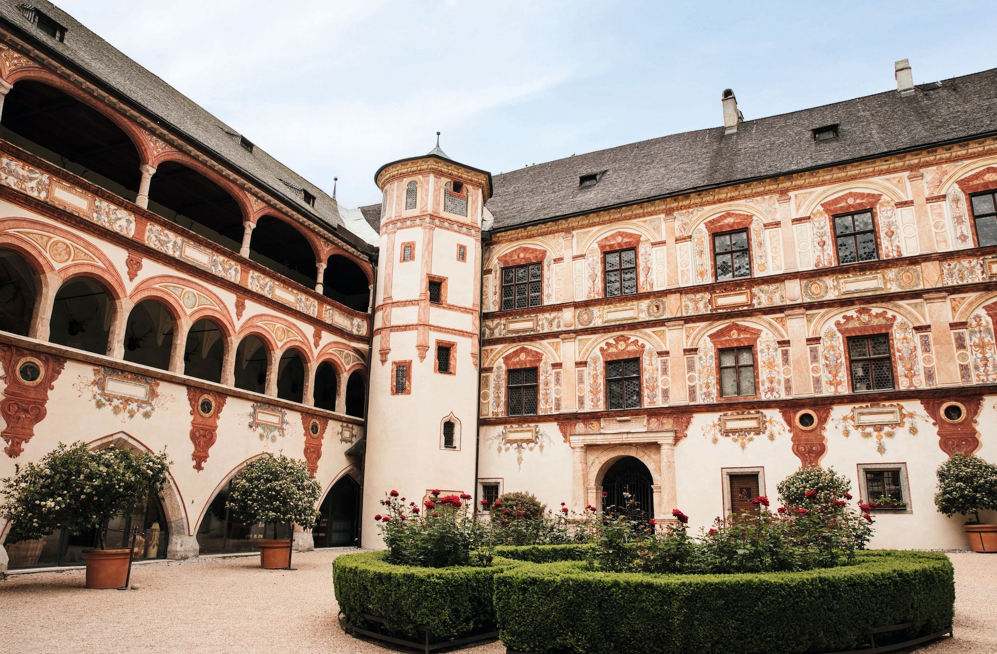 Patio histórico con arcos, ventanas ornamentadas y flores rojas en el centro.