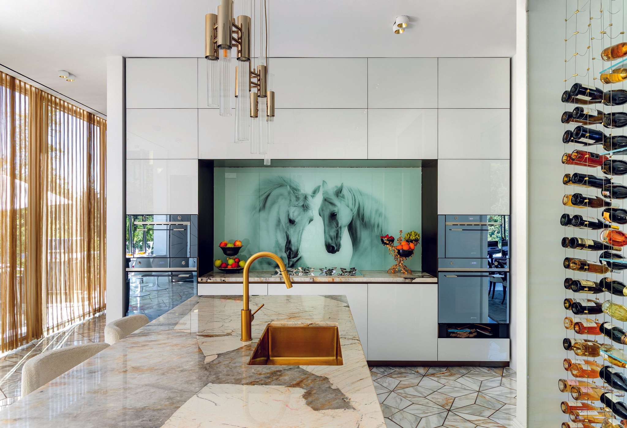 Cocina moderna con encimera de mármol, grifo dorado y mural de caballos.