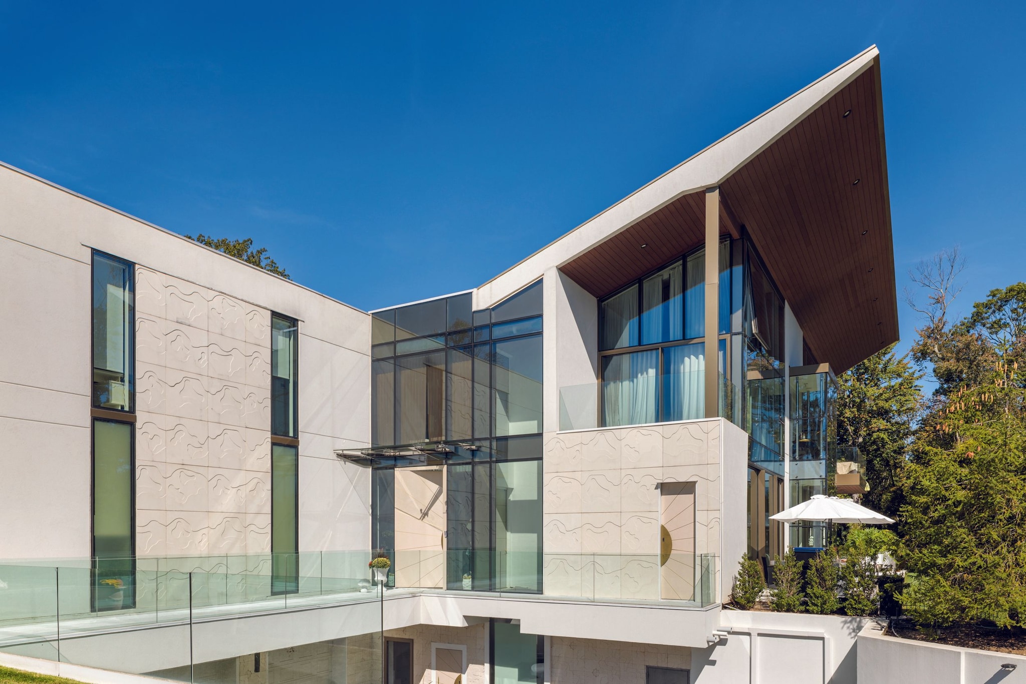 Moderna casa de vidrio con terraza y sombrillas, rodeada de árboles