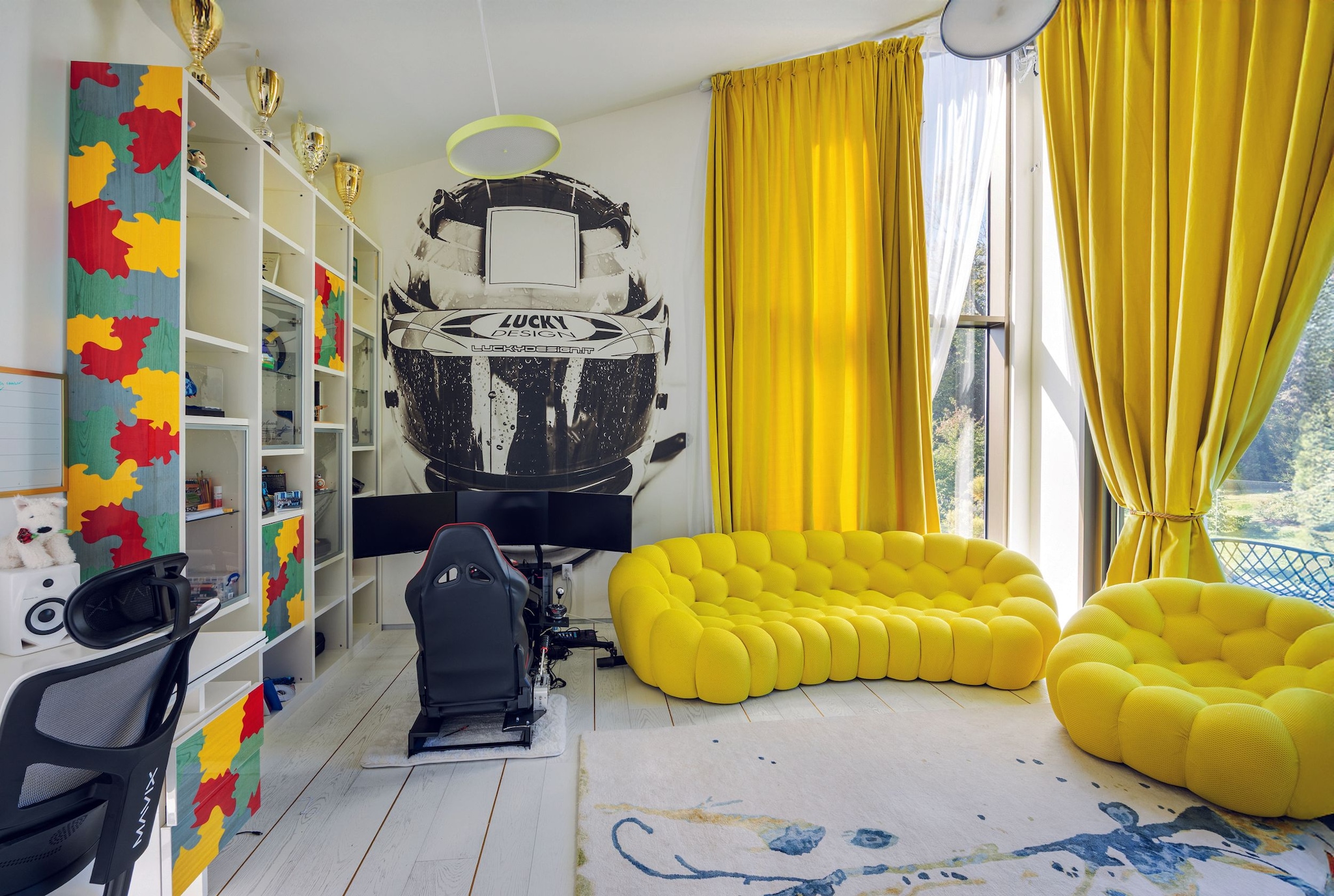 Sala con sofás amarillos, silla de juego, y mural de casco de carreras.