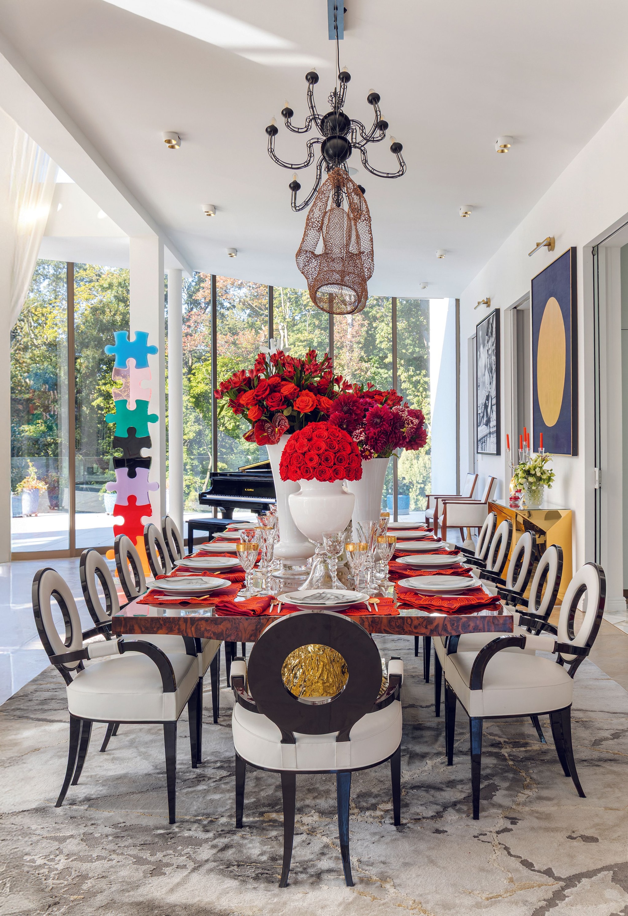 Comedor elegante con mesa larga, flores rojas en jarrones, sillas de diseño y araña de luz.