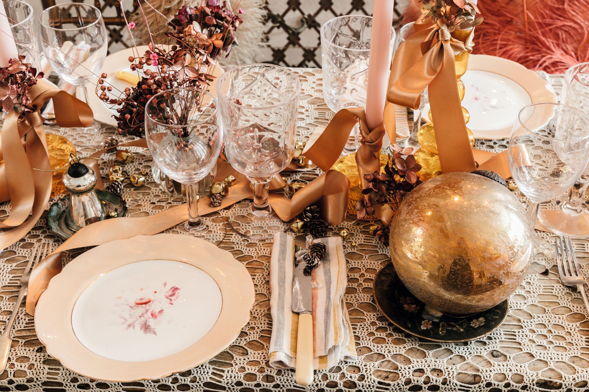 Mesa decorada con mantel de encaje, platos, copas, cubiertos y centros de mesa dorados.