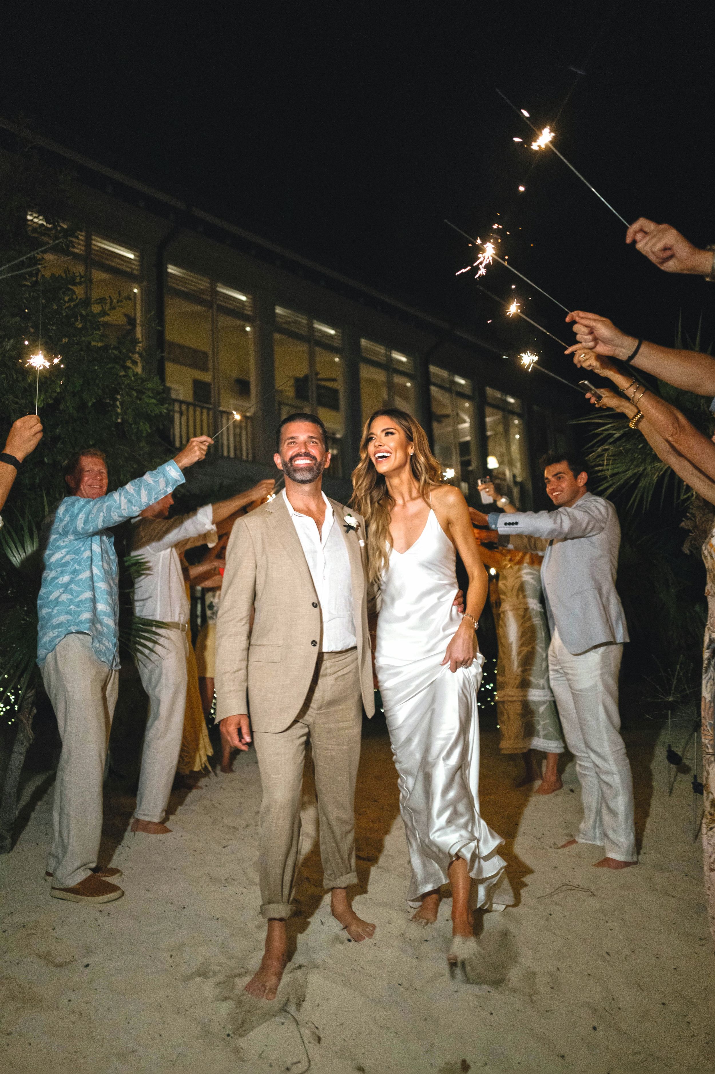 Los novios, descalzos sobre la arena en la playa, reciben las felicitaciones de sus invitados