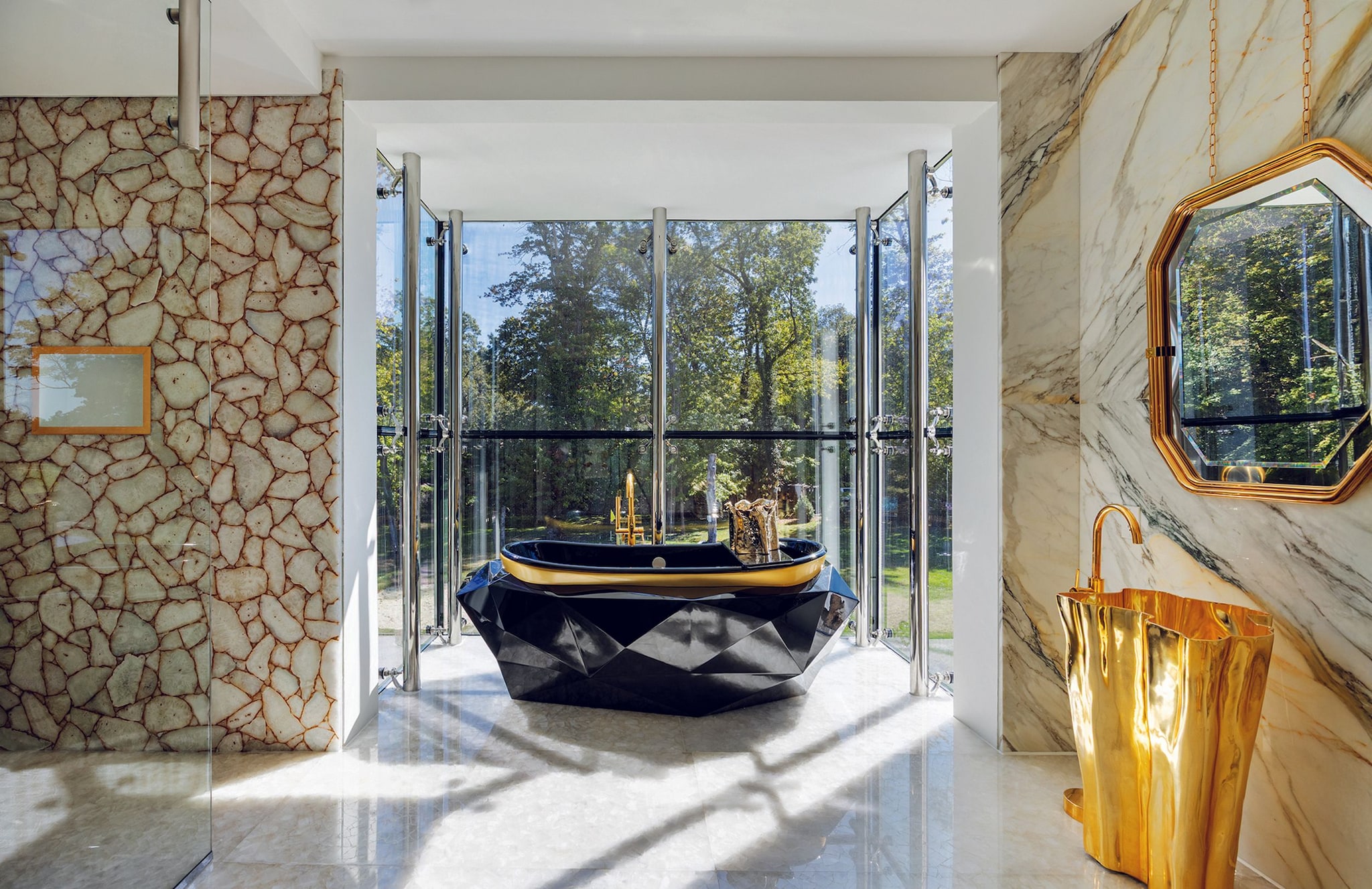 Baño lujoso con bañera negra y dorada, espejo colgante, y vista a árboles.
