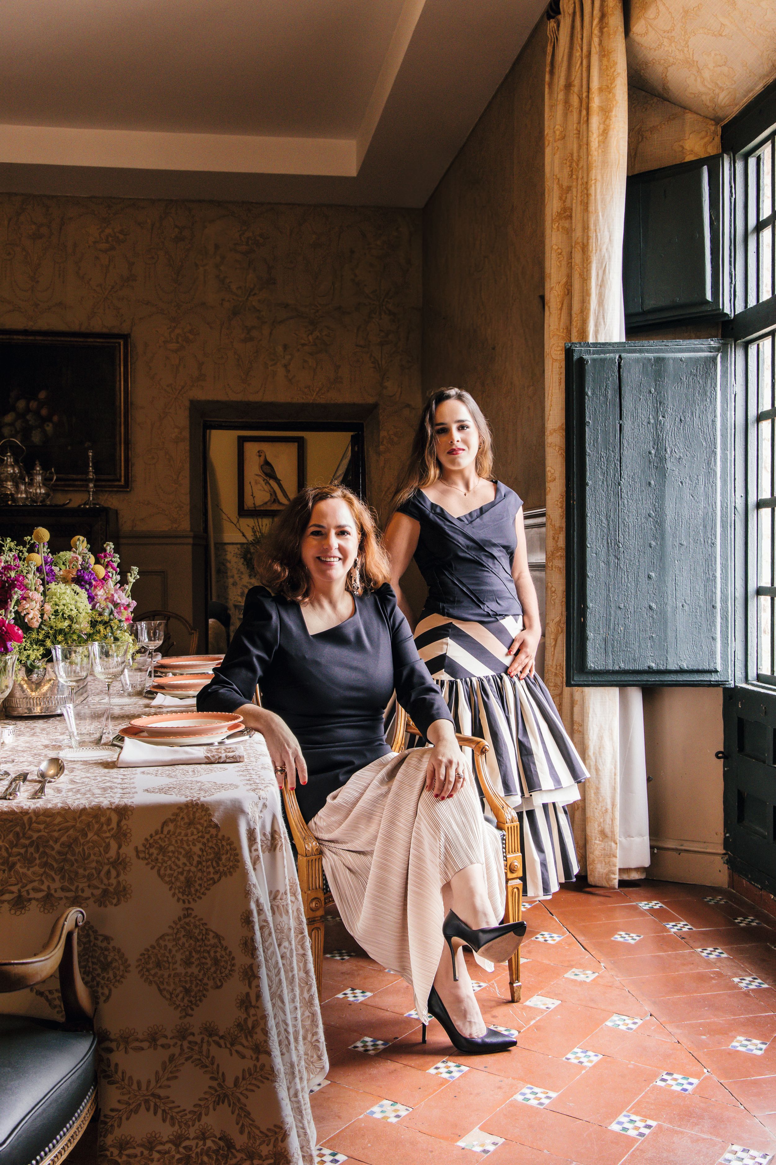 Rita y su hija, que se llama igual, posan en el comedor, con la mesa exquisitamente decorada con mantel de Torres Novas, cubertería de plata de Christofle, vajilla familiar de Limoge Villeroy & Boch, cristalería de Zara Home y decoración floral de The Flower Power