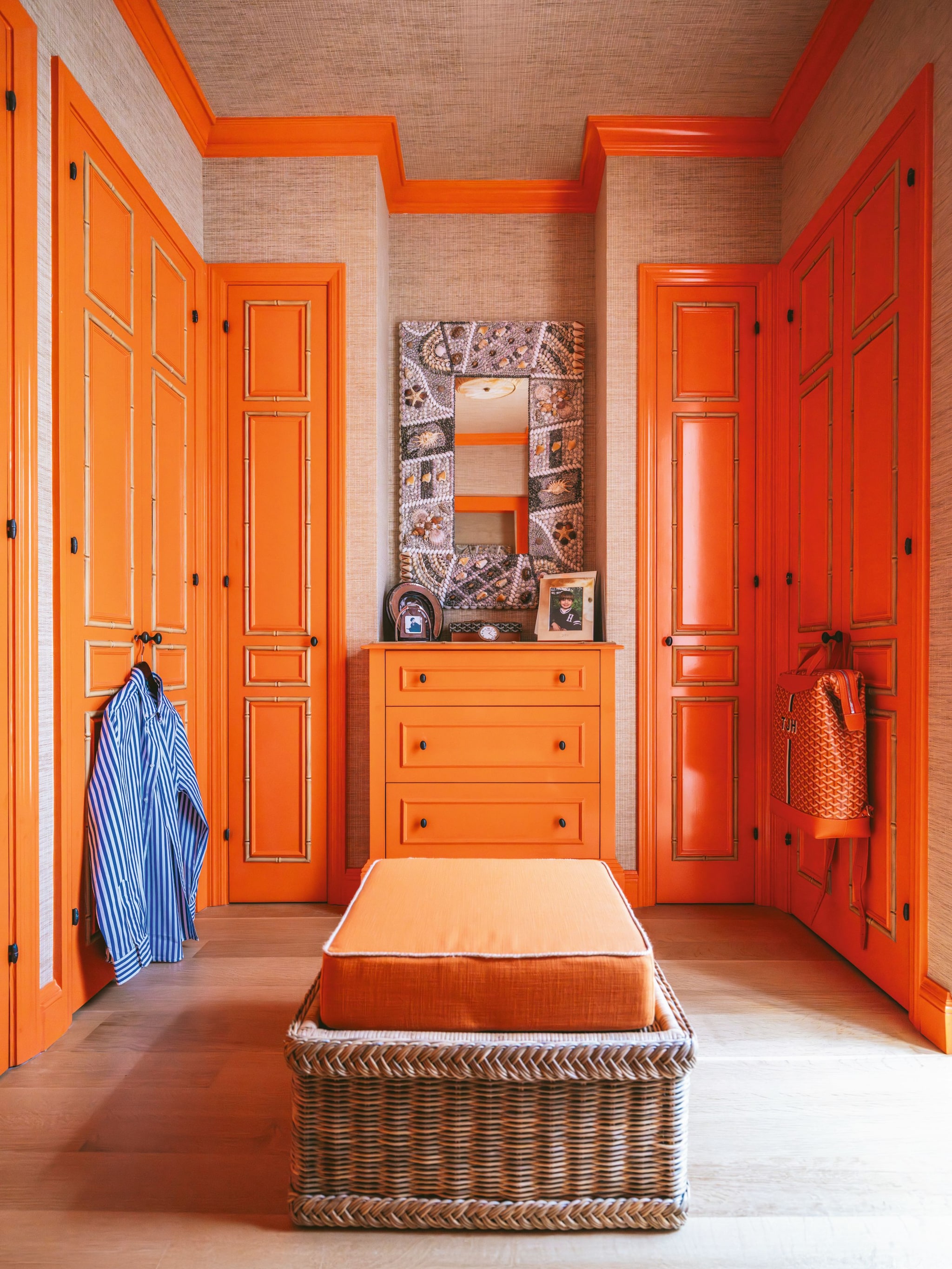 Habitación vestidor con armaros de puertas naranjas , espejo decorativo cómoda y blanco de mimbre